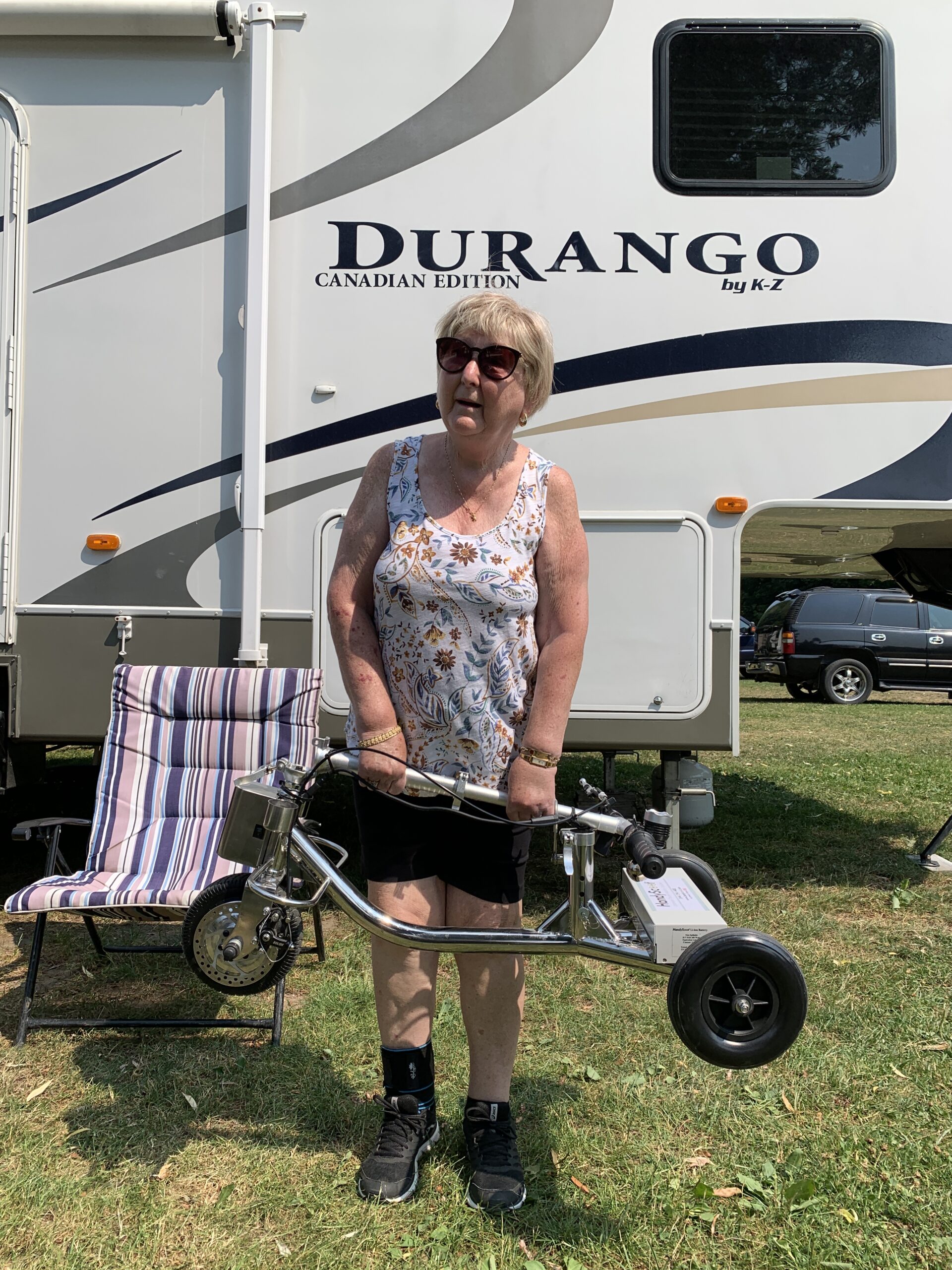 A woman lifting a folded mobility scooter near an RV trailer
